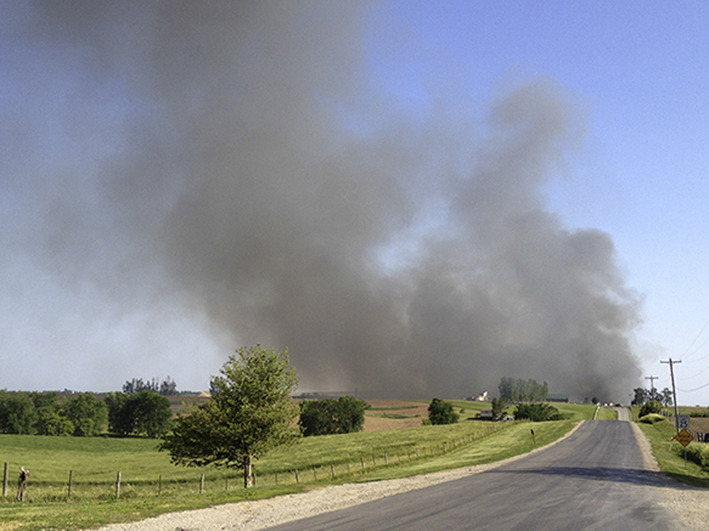 grey smoke in the sky, green pastures below